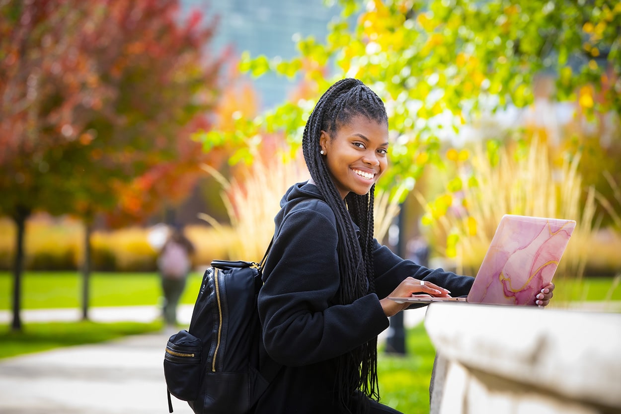 Ryann Sterling (RBS '25) uses her laptop to study on  Livingston campus, outside with fall colors.